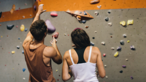 A man and woman stand in front of a rock climbing wall